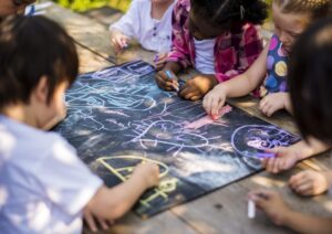 Children draw with chalk outdoors around a picnic table