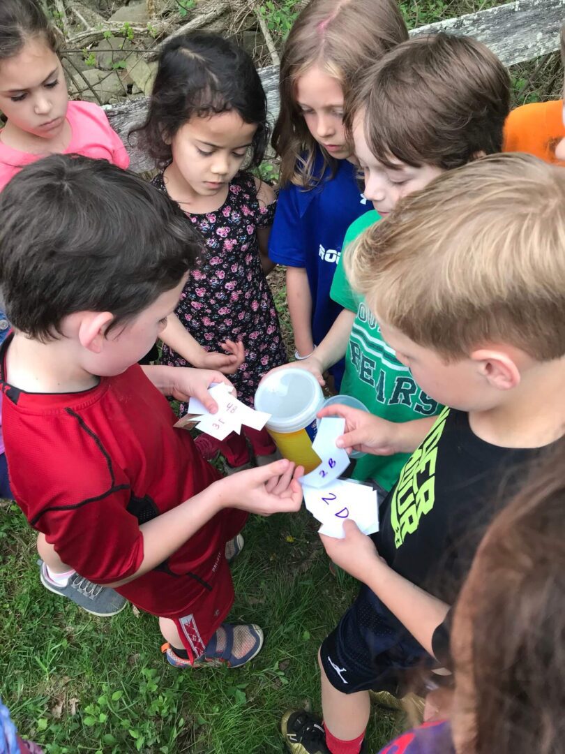 Children gathered outdoors, examining objects closely with curiosity.