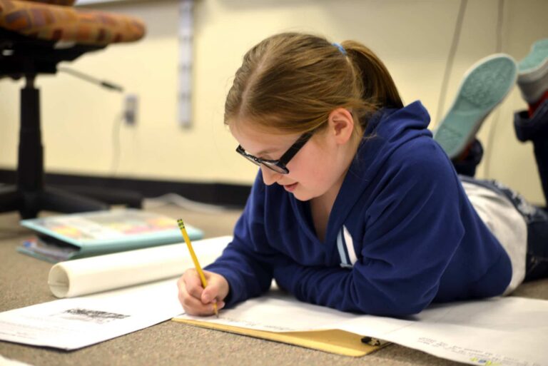 A girl focused on writing in a notebook at a desk.