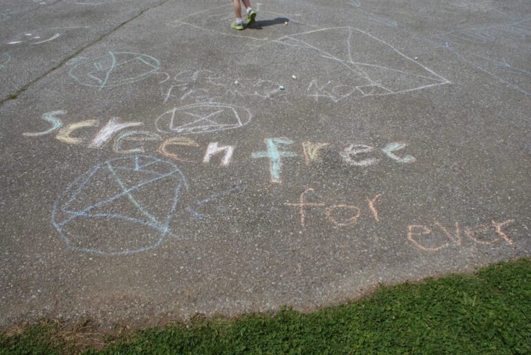 Chalk messages and drawings on pavement with peace symbols and 'freedom' text.