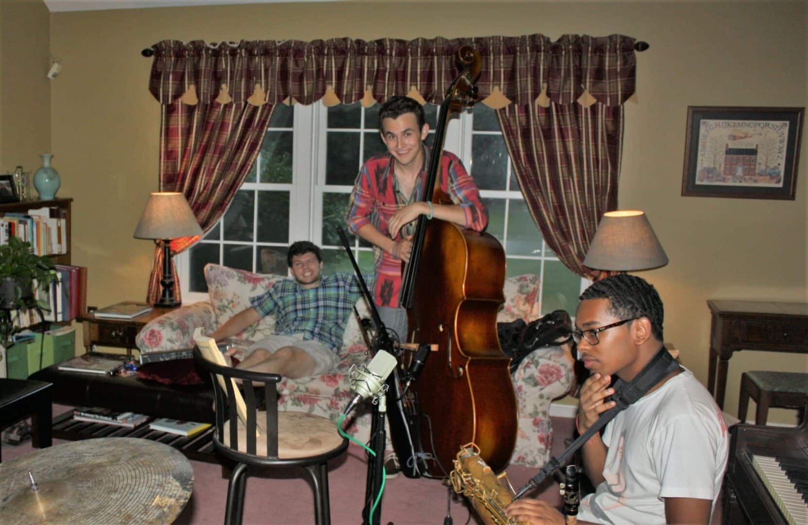 Young man standing with string bass with two others on couch
