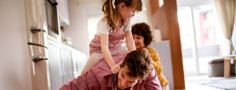 A father playing with his two young children indoors.