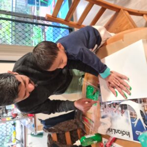 A man helps a young boy with a craft project at a table.