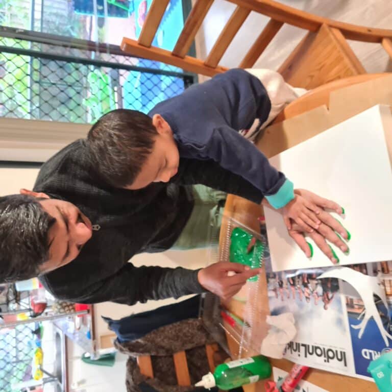 A man helps a young boy with a craft project at a table.