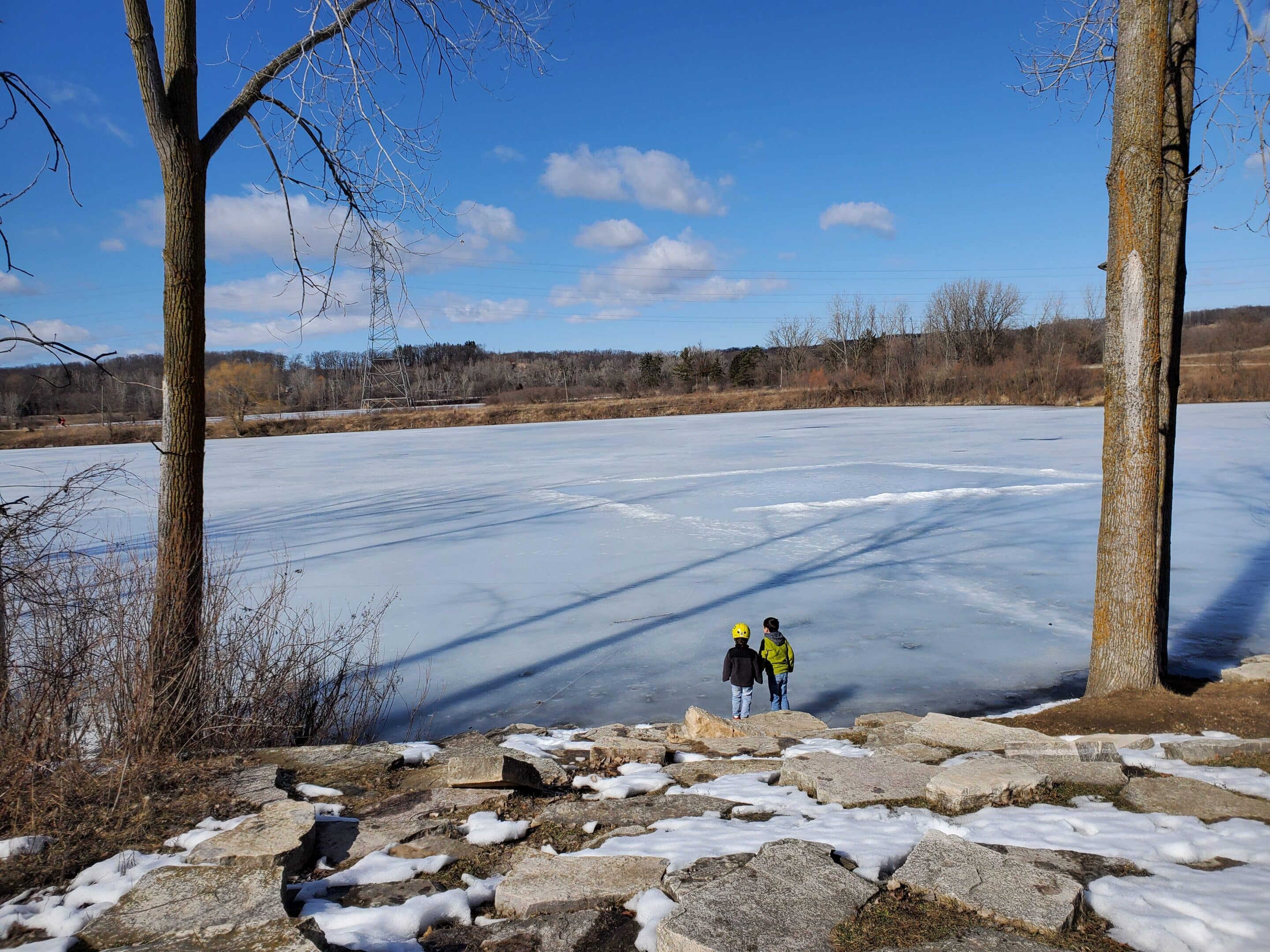 A person crouching near a frozen lake on a sunny winter day.
