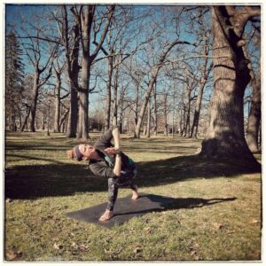 A person doing a yoga pose outdoors in a leafless park.