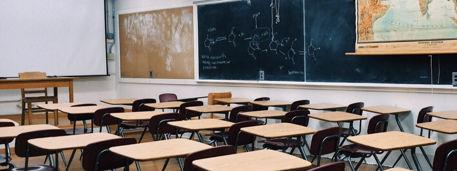 Empty classroom with desks and chalkboards filled with scientific diagrams.