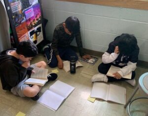 Three students study intently together, surrounded by books and notes.