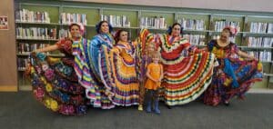 Women and a child in colorful traditional dresses posing indoors, likely at a cultural event.