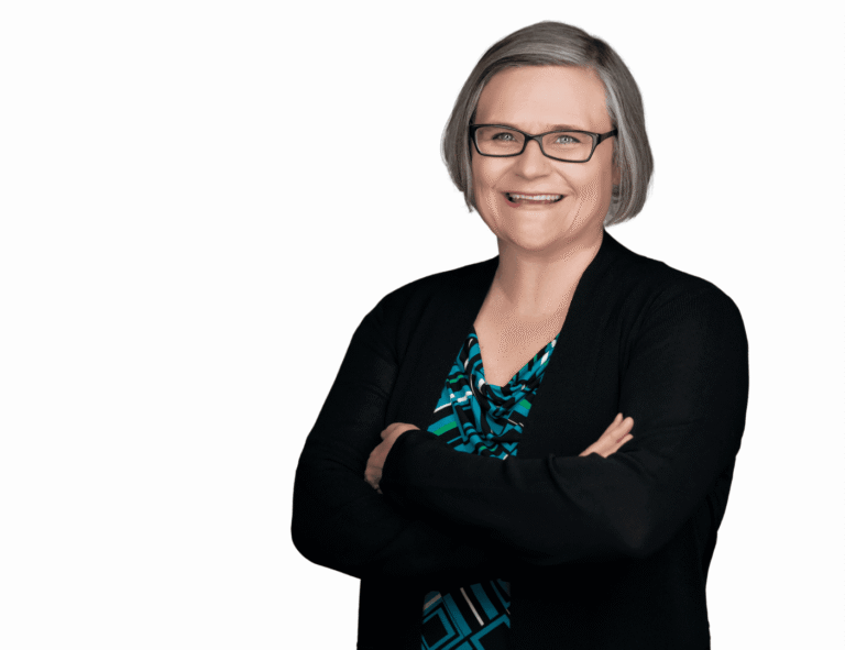 Smiling woman with glasses and crossed arms in business casual attire.