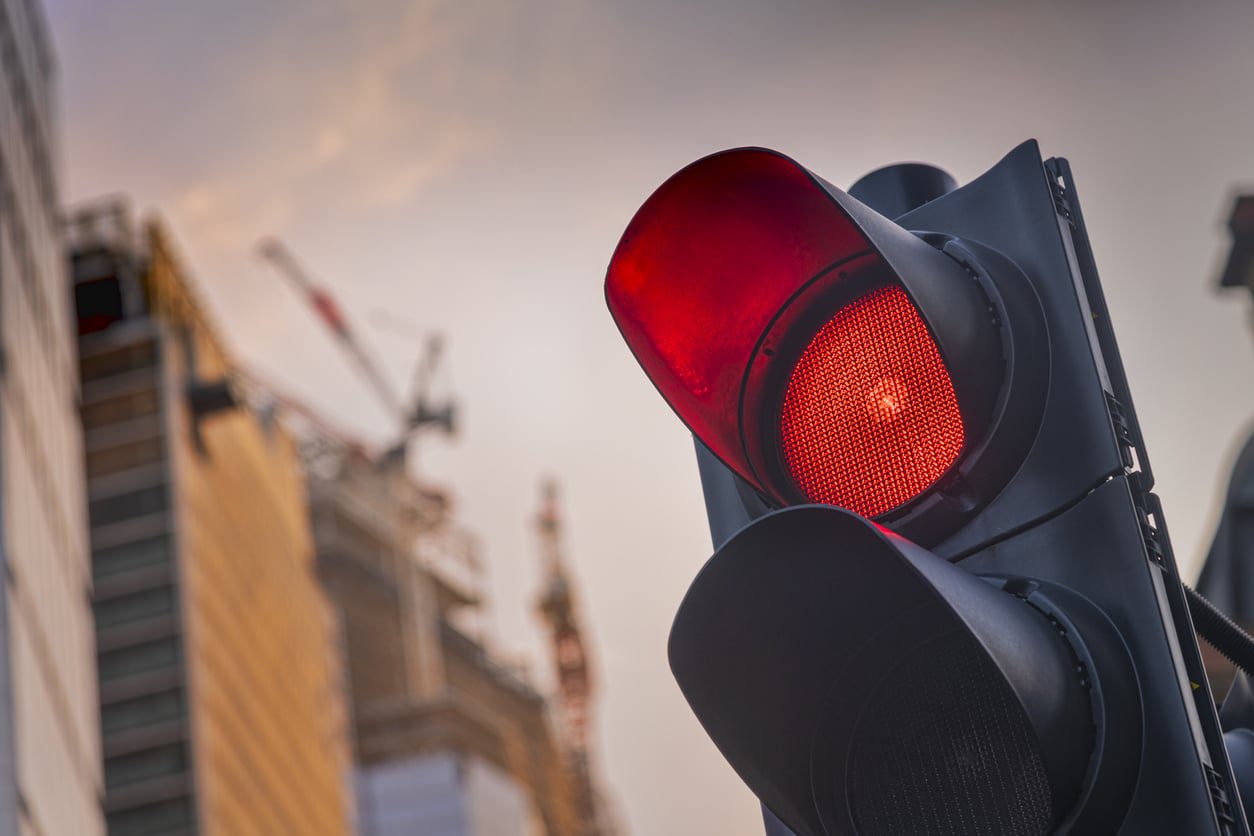 Close-up of a red traffic light against a blurred construction background.
