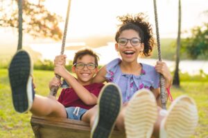 Two joyful children swinging outdoors on a sunny day.