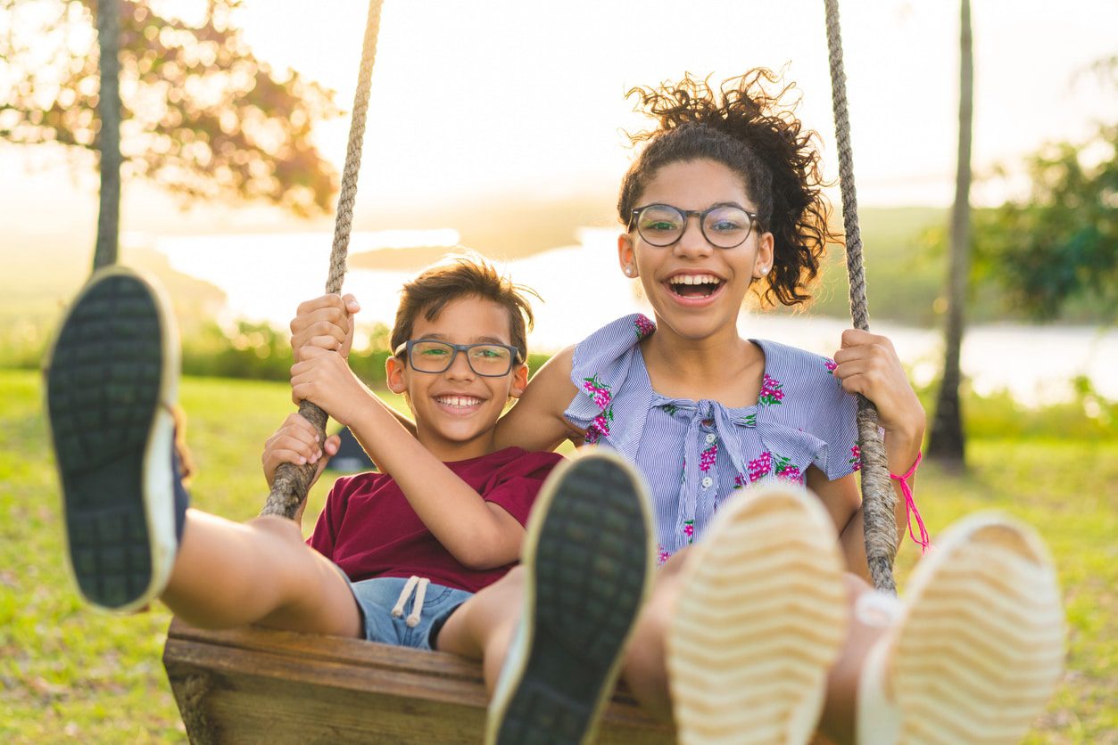 Two joyful children swinging outdoors on a sunny day.