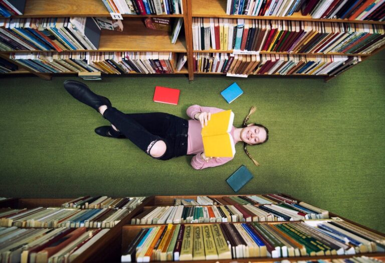 Person lying on library floor surrounded by books and shelves.