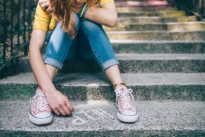Person sitting on stairs tying shoelaces on floral sneakers.