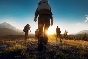 Three hikers walking towards the sunrise on a trail.