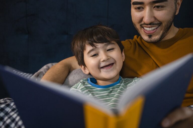 A father reading a book to his smiling son.