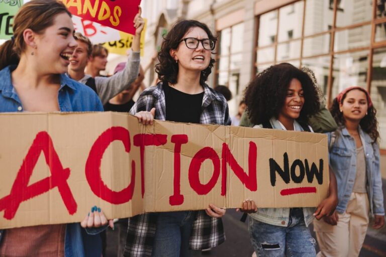 Protesters holding a large sign reading 'Action Now' during a demonstration.
