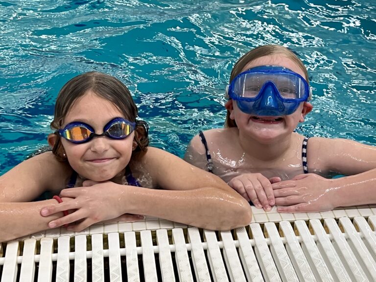 Two kids smiling in a swimming pool with goggles.