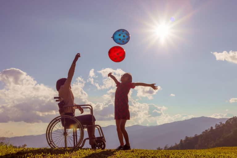 Two boys playing catch outdoors, one in a wheelchair.